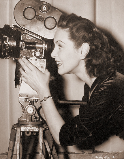 Patricia Roc behind the camera for a change, takes a look through the view finder to observe the scene from her fiance Andre Thomas’s viewpoint – he is an expert French cameraman.    They will be married in the spring of this year.  An off-set shot from The Perfect Woman, the Two Cities film version of the successful comedy, starring Patricia Roc with Stanley Holloway and Nigel Patrick, produced by George and Alfred Black and directed by Bernard Knowles at Denham.  
