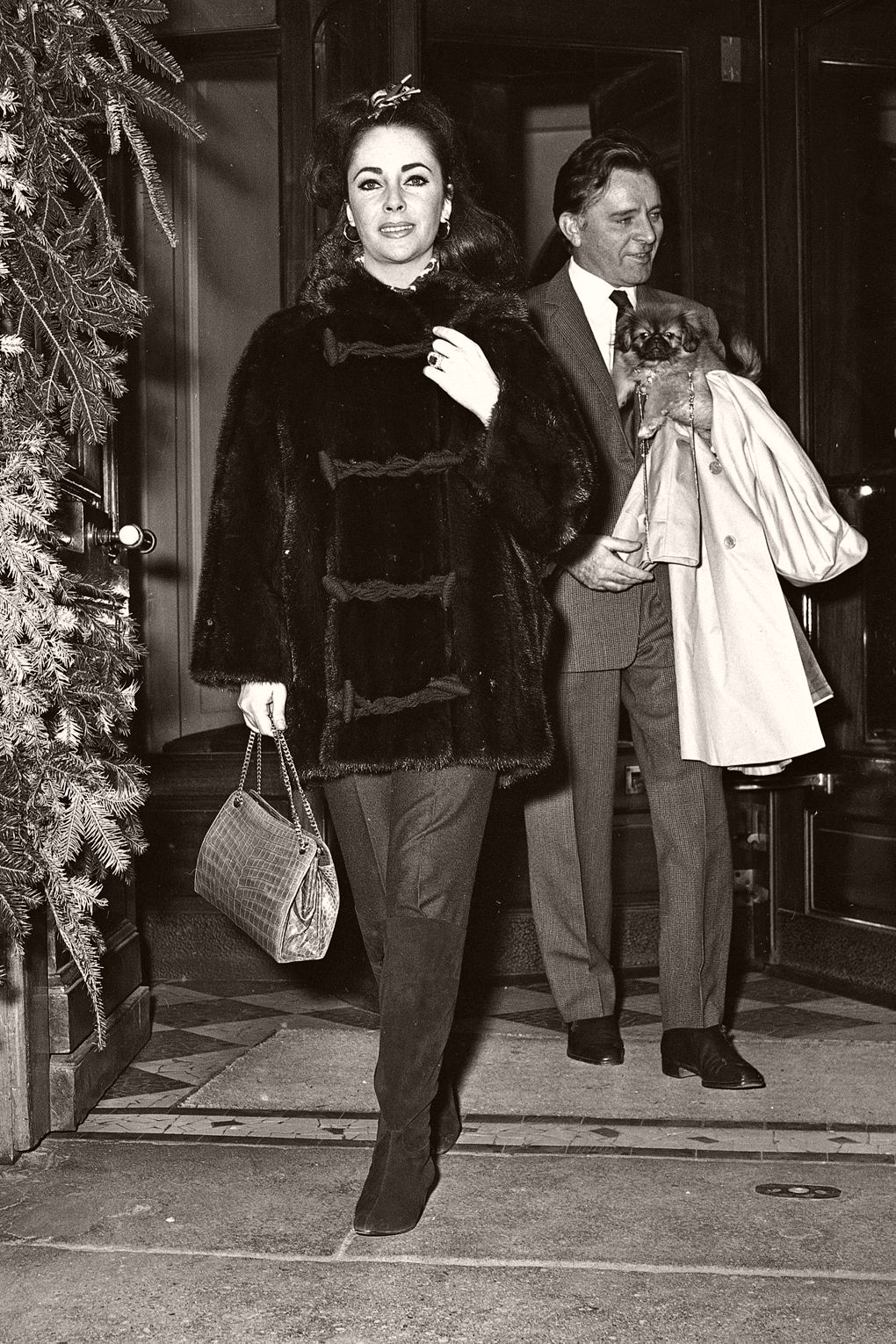 Elizabeth Taylor married Richard Burton in March 1964 and they adopted their daughter Maria that same year. Here, the couple are pictured at the Lancaster Hotel in Paris, where they spent Christmas with their children. Taylor is wearing a $6,000 mink ski jacket from Chombert as she strides past a Christmas tree towards the camera. Burton in the background holds a dog in his arms