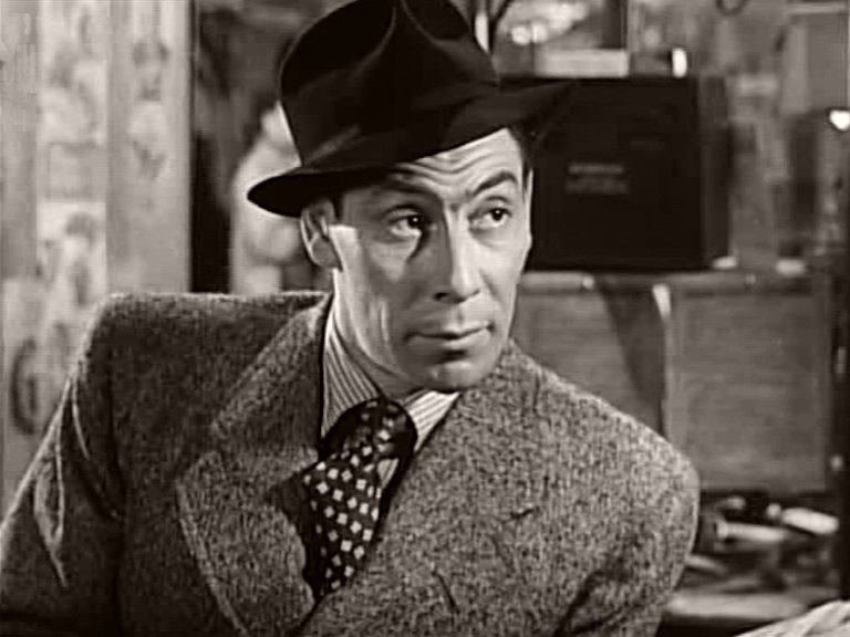 Lou (John Slater) in overcoat, tie and hat in a scene from It Always Rains on Sunday (1947)