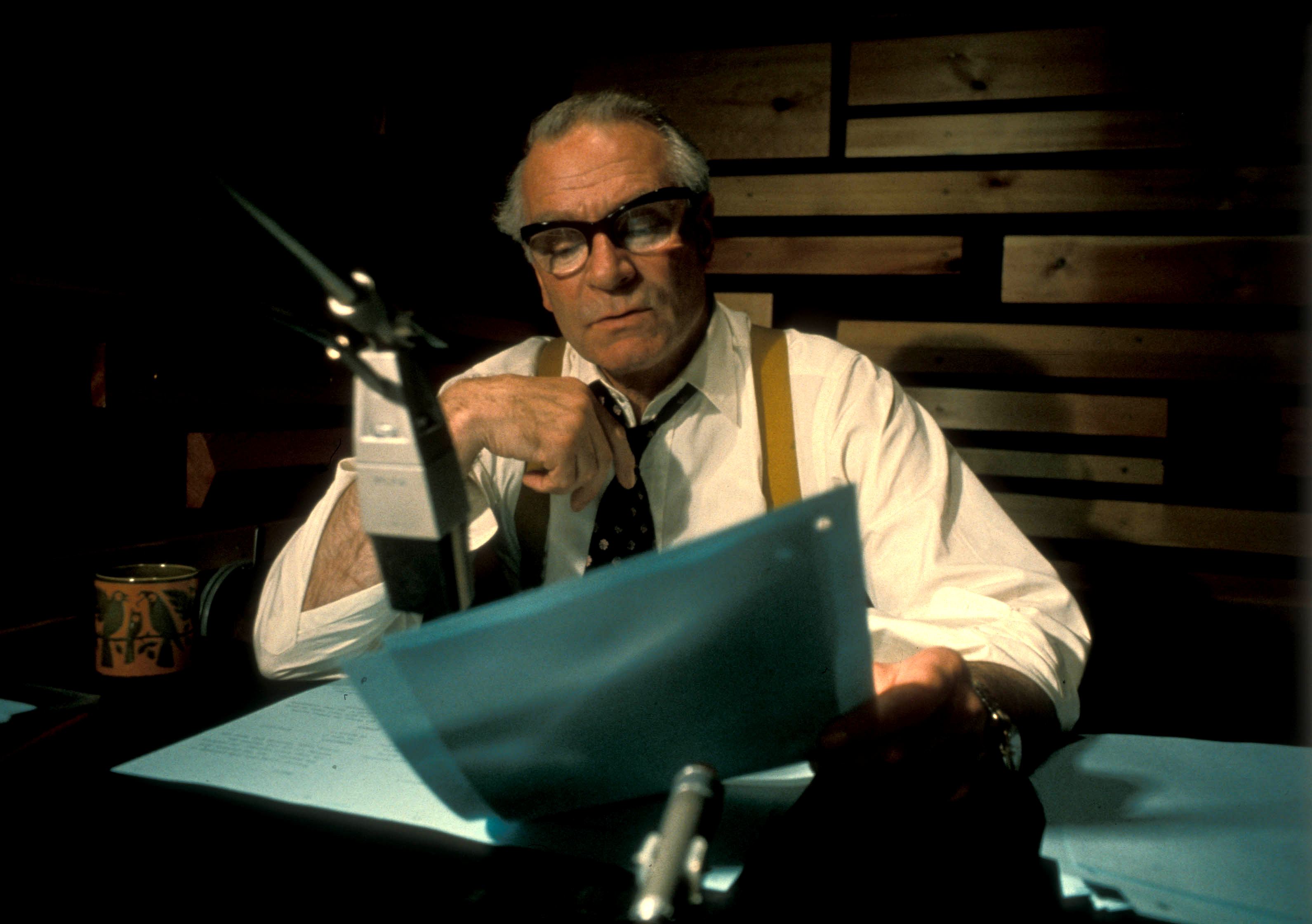 Photo of Laurence Oliver narrating The World at War (1973-4). The actor is in rolled-up shirt sleeves while reading the script in front of a microphone
