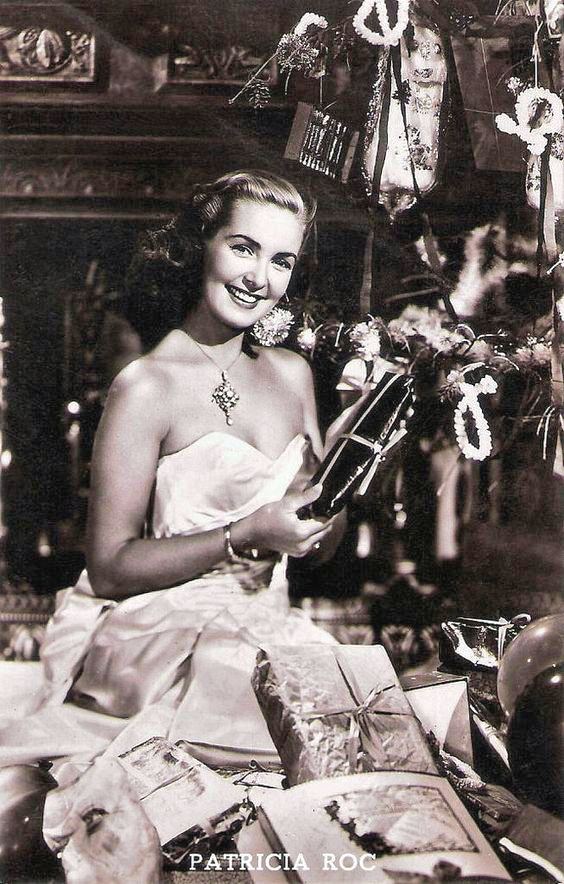 British actress Patricia Roc sits wears an off-the-shoulder dress as she sits in front of a real fire  Roc is surrounded by Christmas presents and decorations