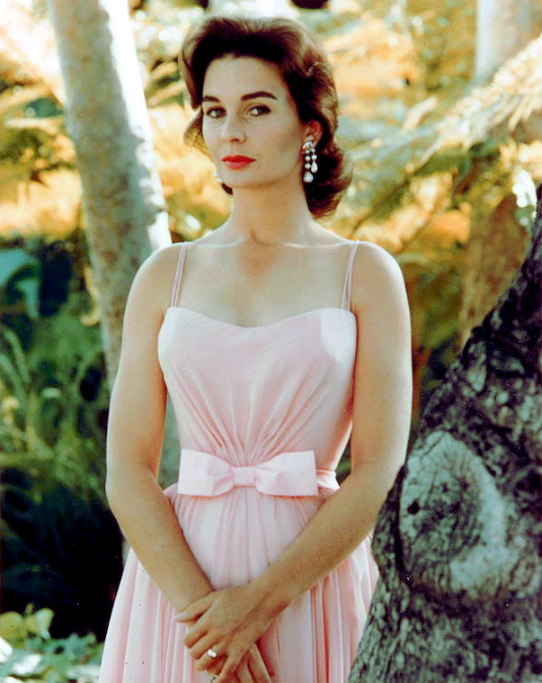 Beautiful Jean Simmons looks demure in a pink dress.   Behind her is sunny woodland.