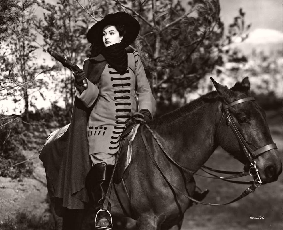 Photograph from The Wicked Lady (1945) (48) featuring Margaret Lockwood (as Barbara Worth). The behatted highwaywoman sits astride a horse and brandishes a pistol