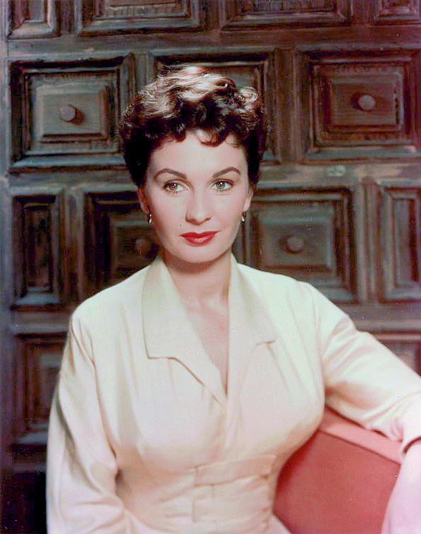 Jean Simmons sits in front of wood panelling